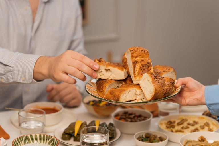 Hands exchanging fresh bread at a dinner table filled with diverse dishes and drinks.