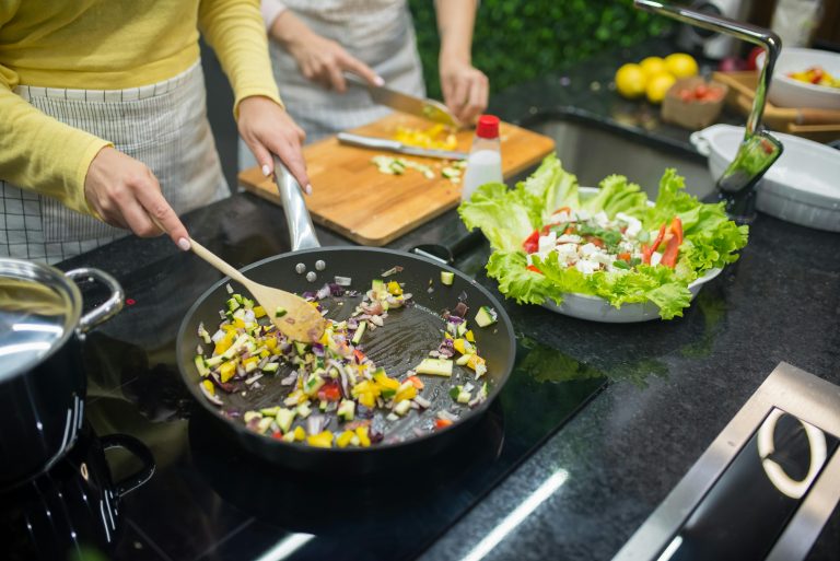 Two adults cooking fresh vegetables on a stove, preparing a healthy meal in a modern kitchen.