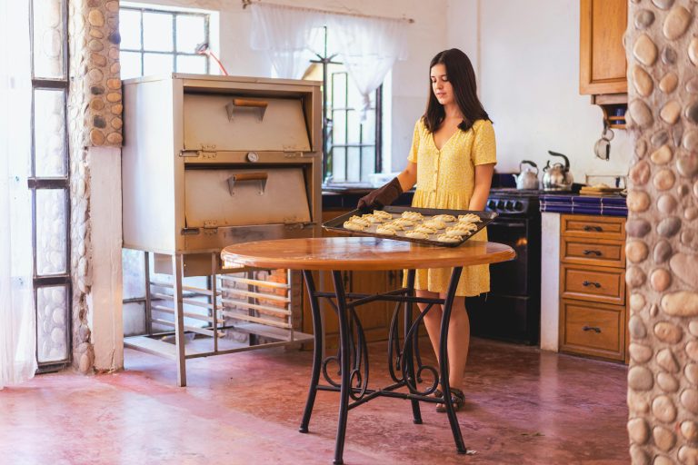 A young woman prepares homemade empanadas on a tray in a cozy, rustic kitchen setting.